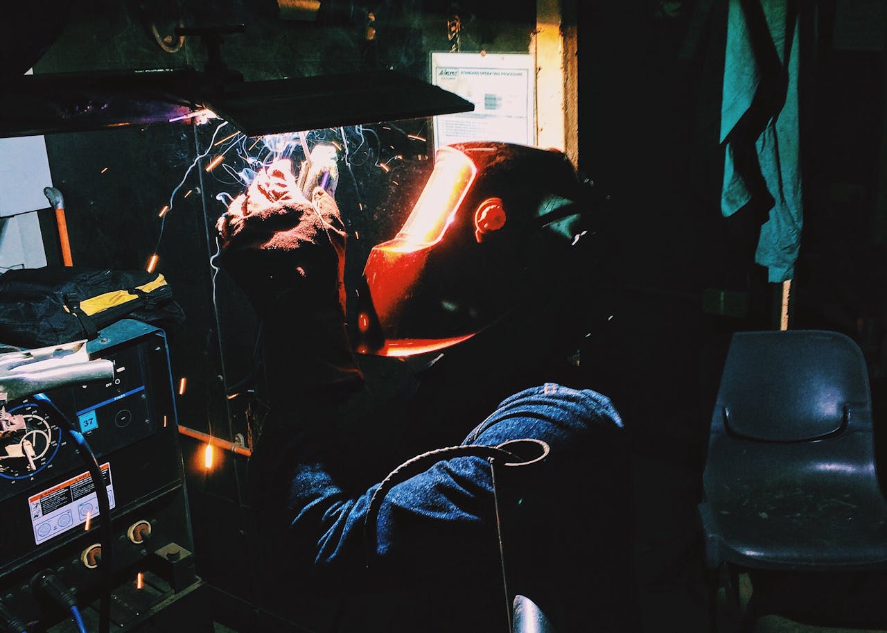 Welder using welding machine with sparks flying in an industrial environment.